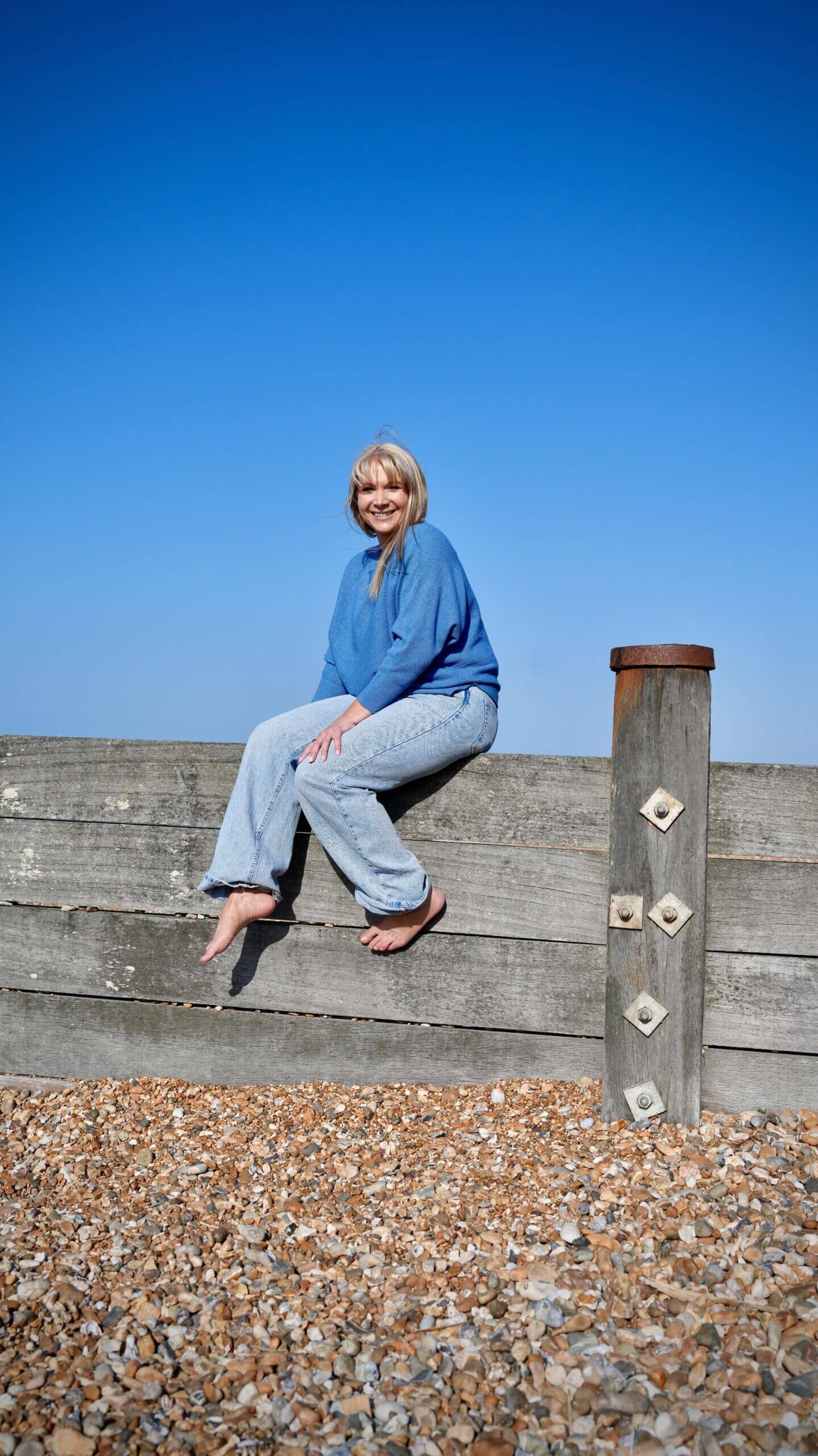 Becky Stone | Therapist Specialising in Eating Disorders and Neurodivergent Support Becky Stone smiling by a wooden beach fence under blue skies, reflecting on ADHD and eating disorder recovery