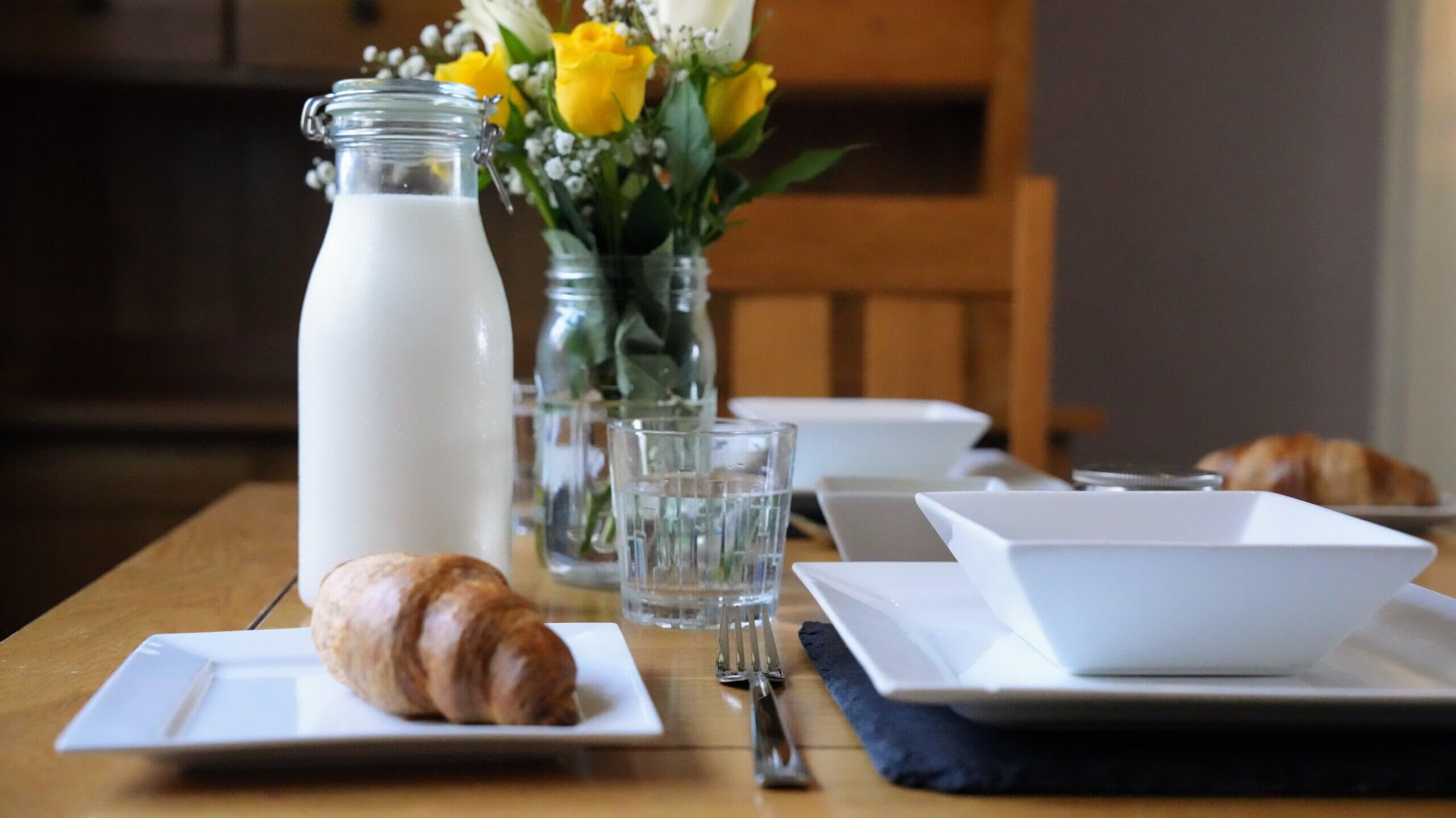 Calm kitchen table with a bottle of milk, croissant, glass of water, and fresh yellow and white flowers