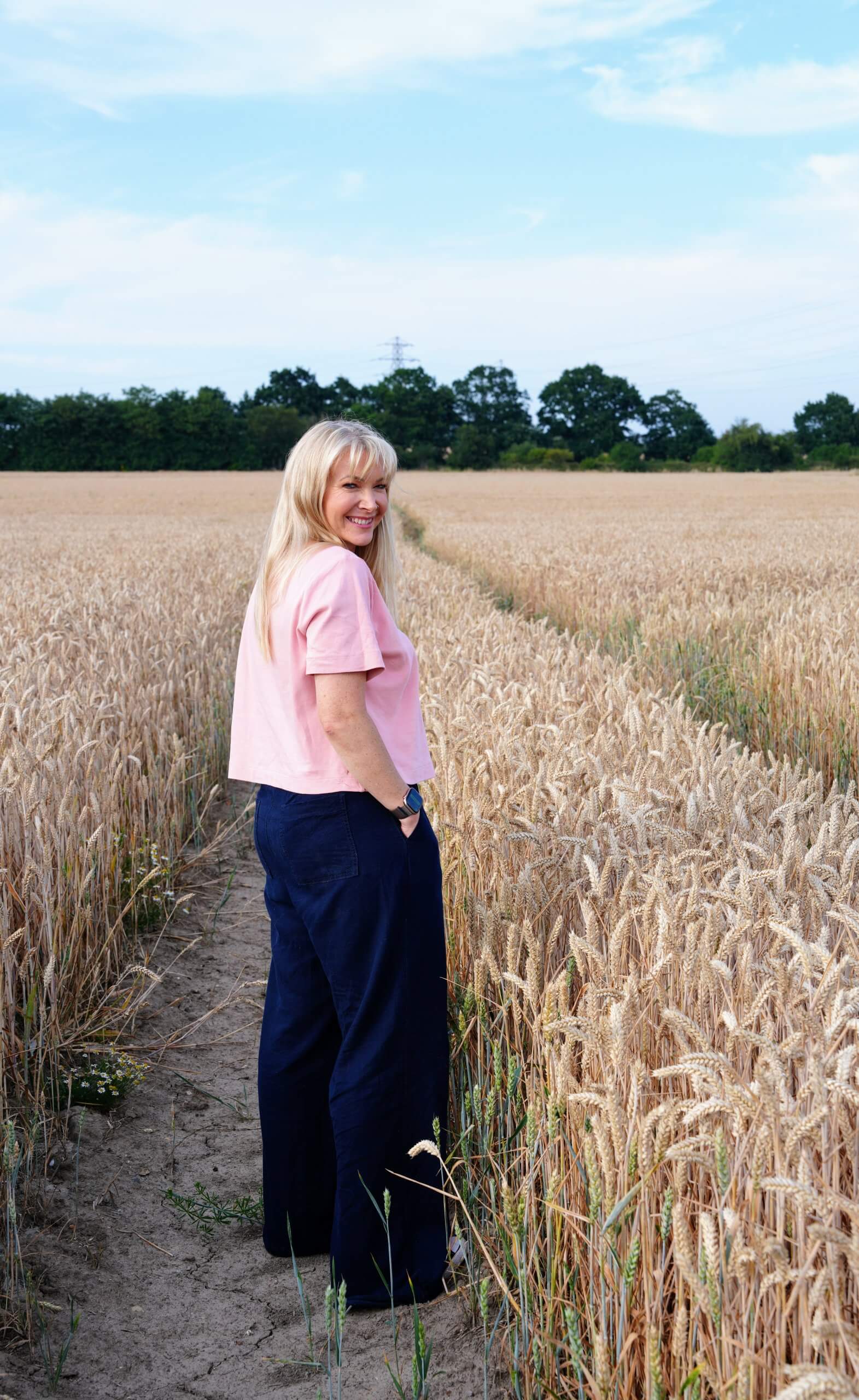 Rebecca Stone walking through a wheat field near Canterbury, smiling at the camera.